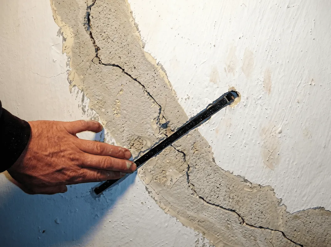 A wall with a large crack is being inspected by a professional in Toledo, OH